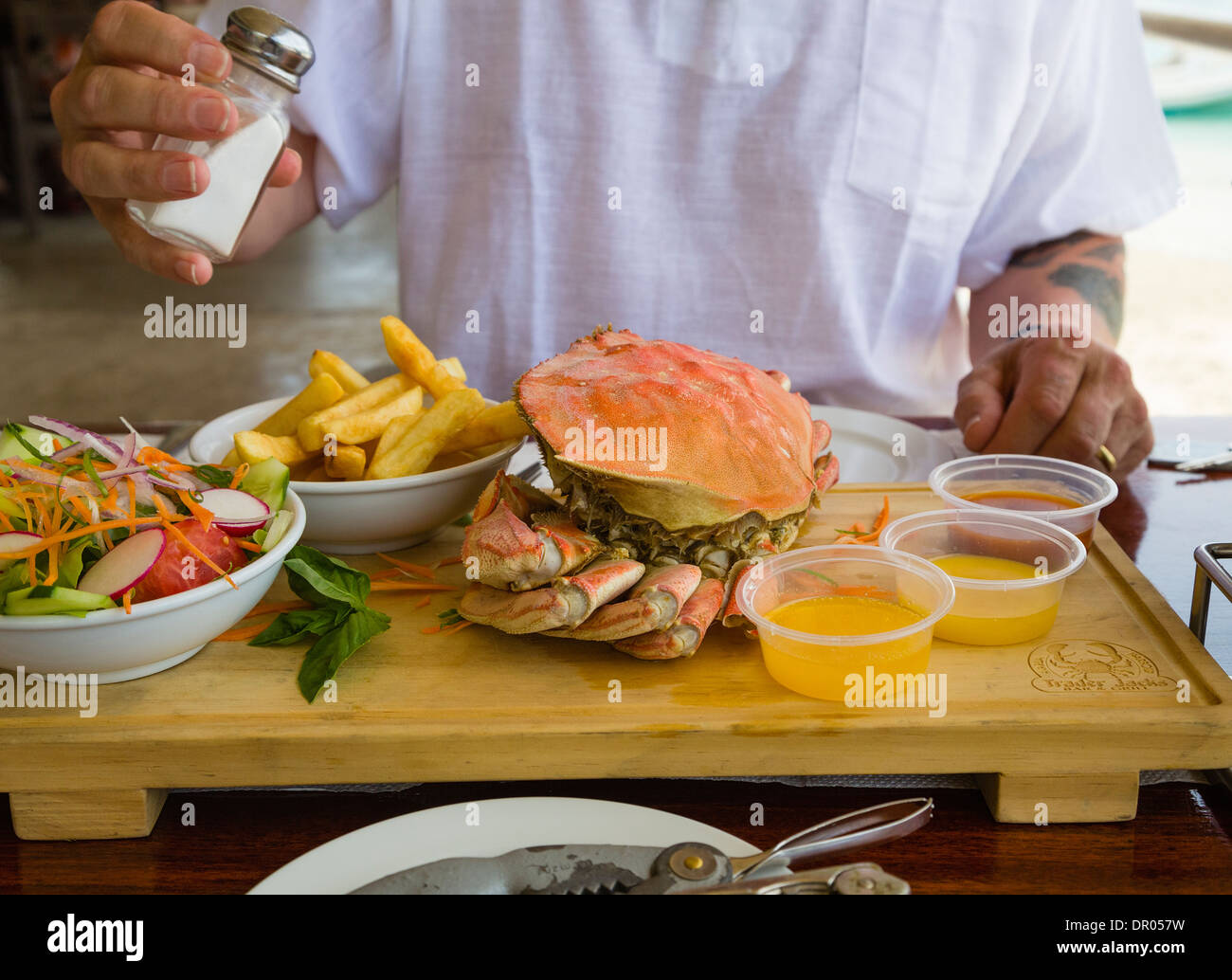A man about to eat a meal of a freshly cooked whole crab, chips and salad with melted butter and dips. Rarotonga, Cook Islands. Stock Photo