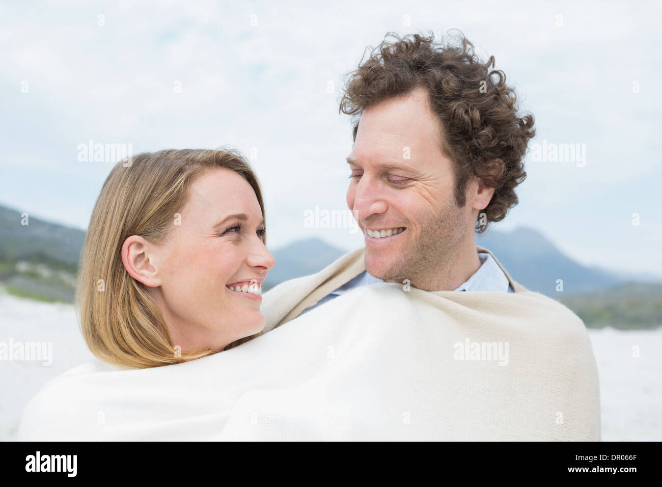 Smiling couple wrapped in blanket at beach Stock Photo - Alamy