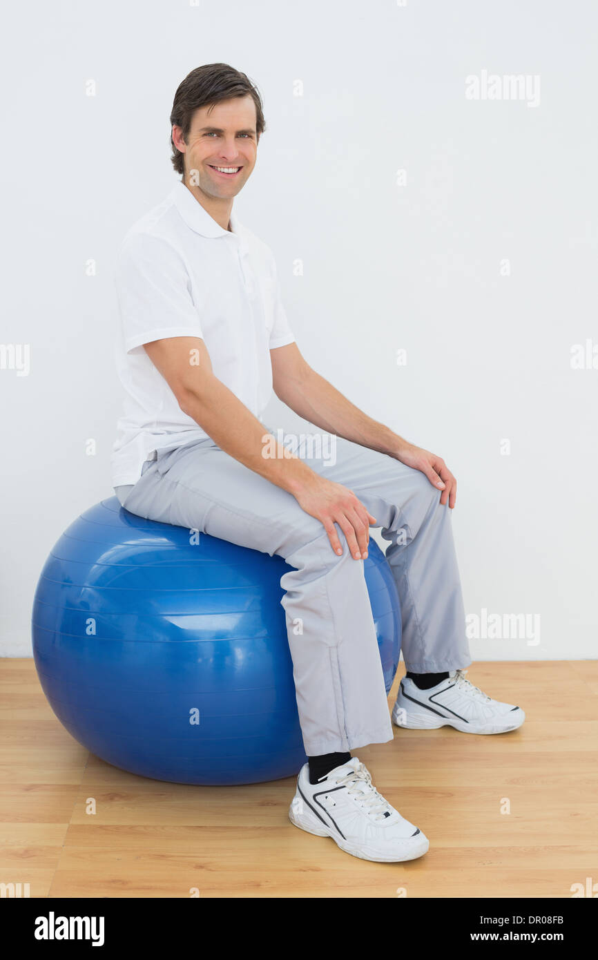 Smiling man sitting on exercise ball in hospital gym Stock Photo