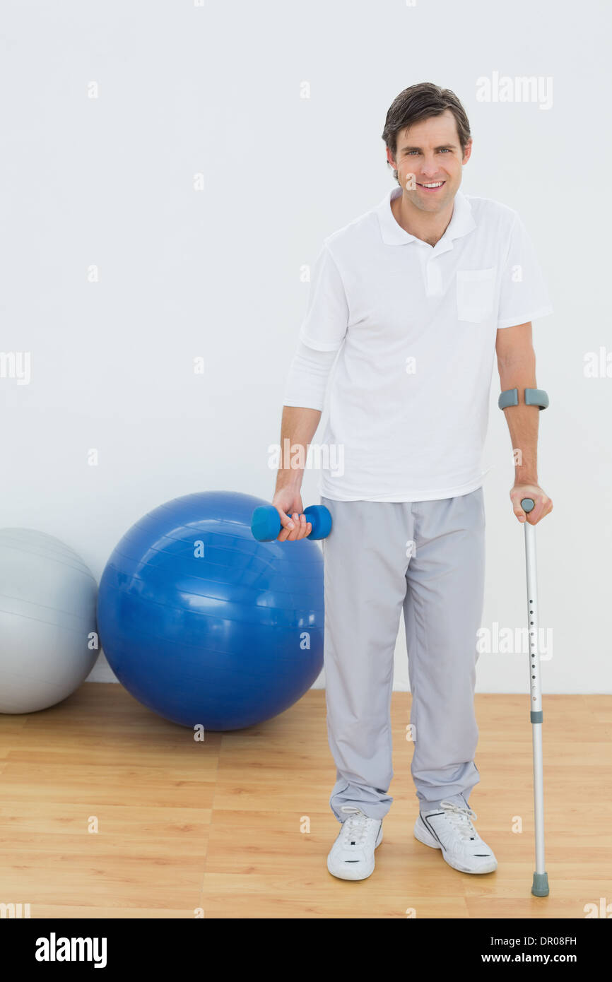 Portrait of a smiling man with crutch and dumbbell Stock Photo