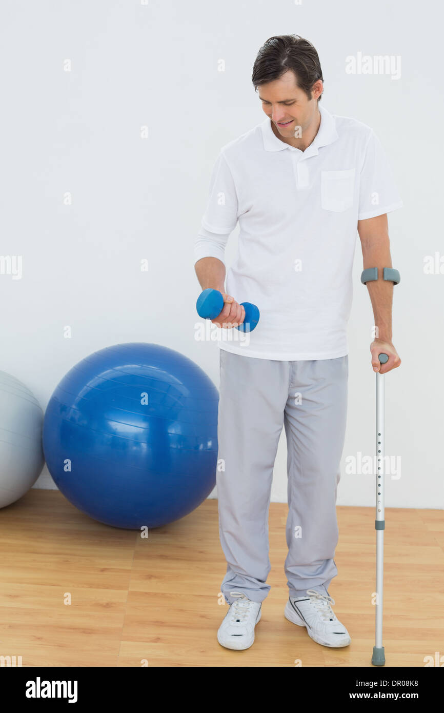 Smiling young man with crutch and dumbbell Stock Photo