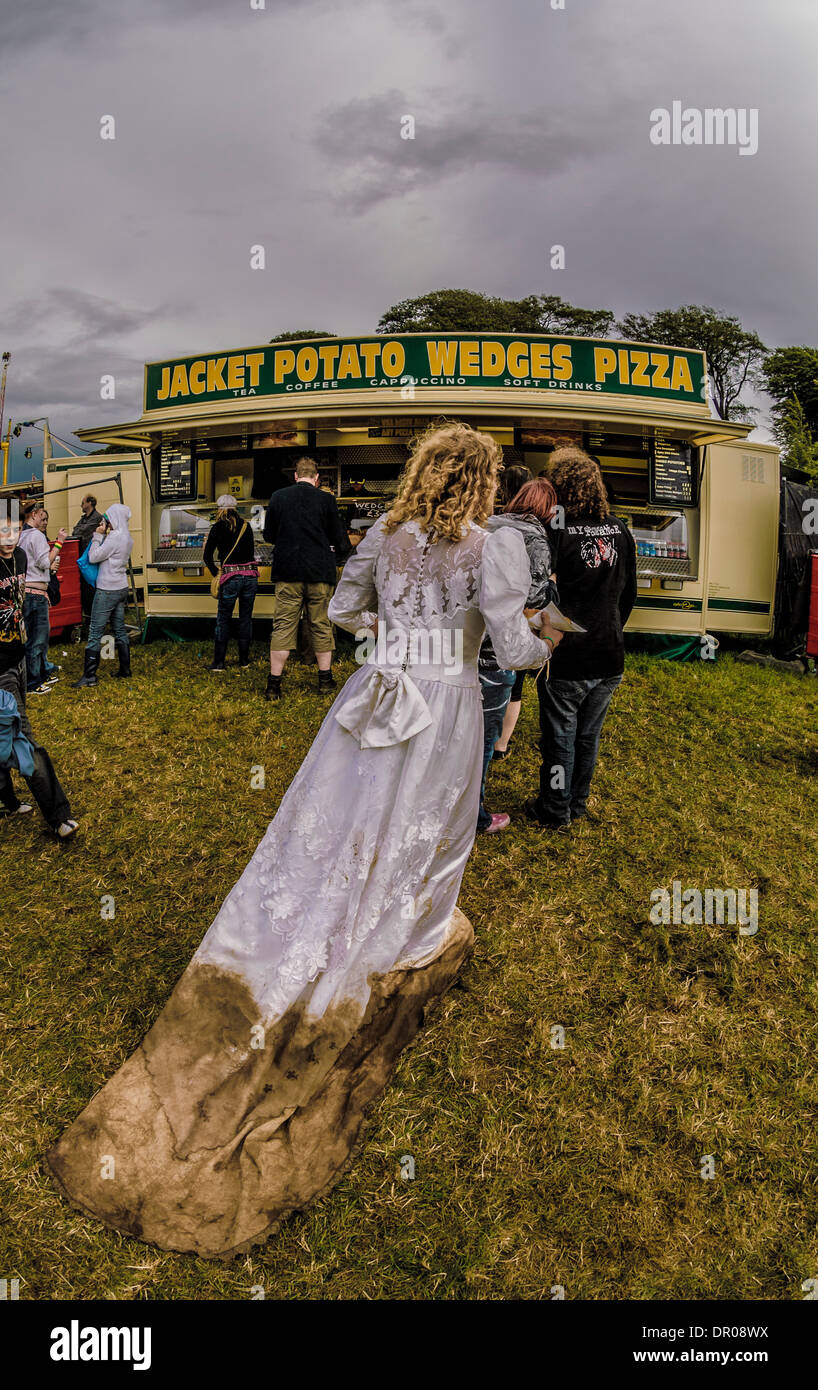 rear view of a an wearing wedding dress with a muddy skirt queuing at a food stall, at a summer music festival. Leeds UK Stock Photo