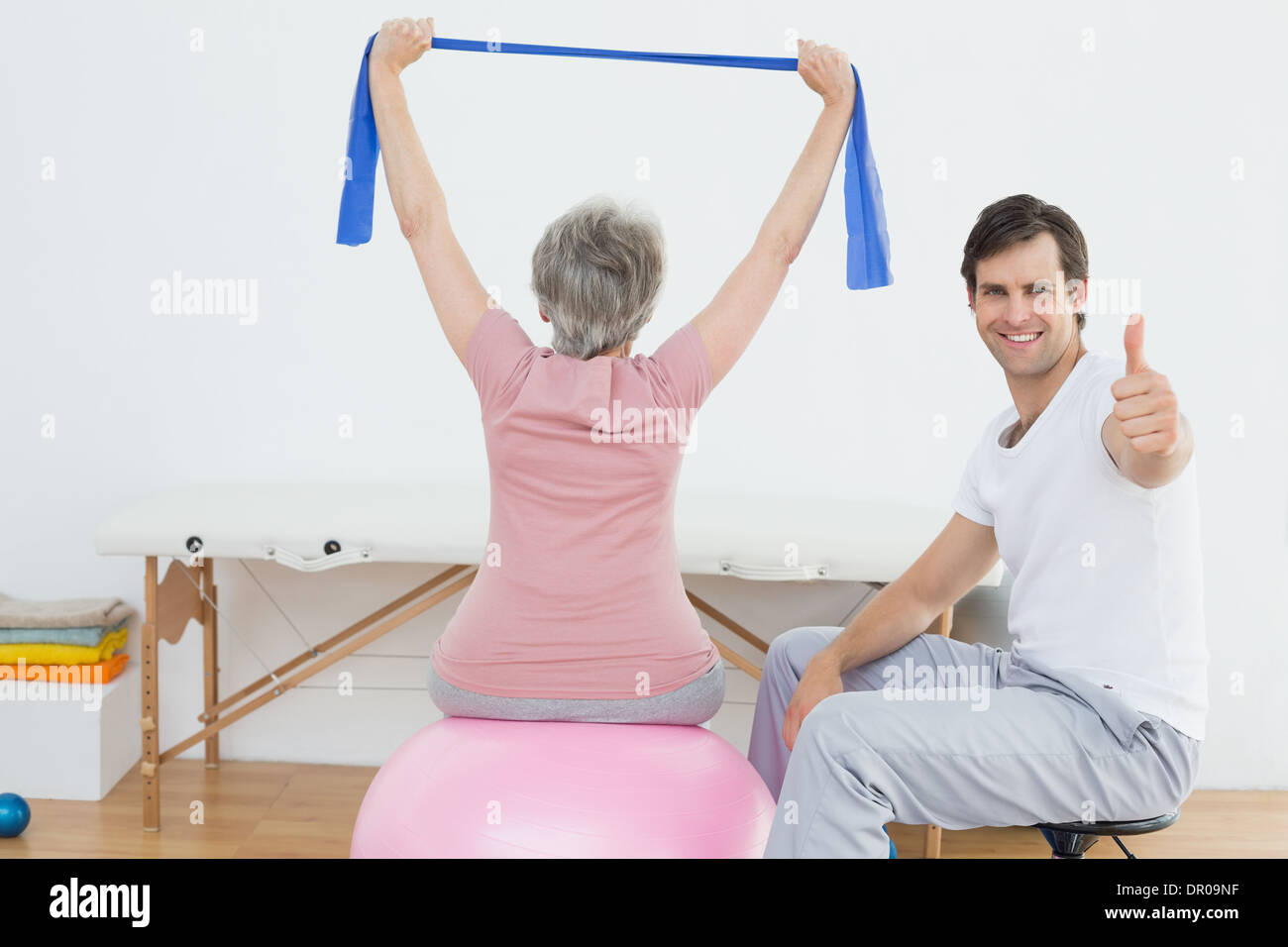Therapist gesturing thumbs up by woman on yoga ball Stock Photo