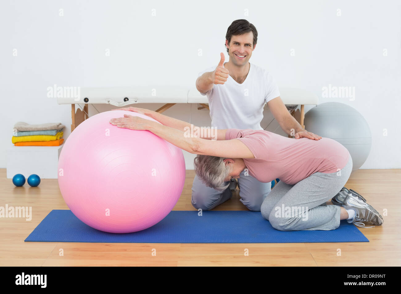 Therapist gesturing thumbs up by senior woman with yoga ball Stock Photo