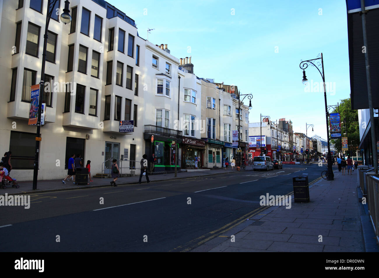 People walk past buildings in the shade along Queens Road in Brighton, East Sussex, UK, on a early summer's evening. Stock Photo