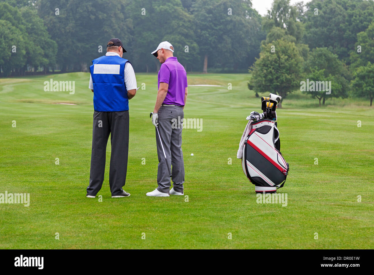 Golfer and caddy on the fairway of a par 4 reading the course guide for club selection. Stock Photo