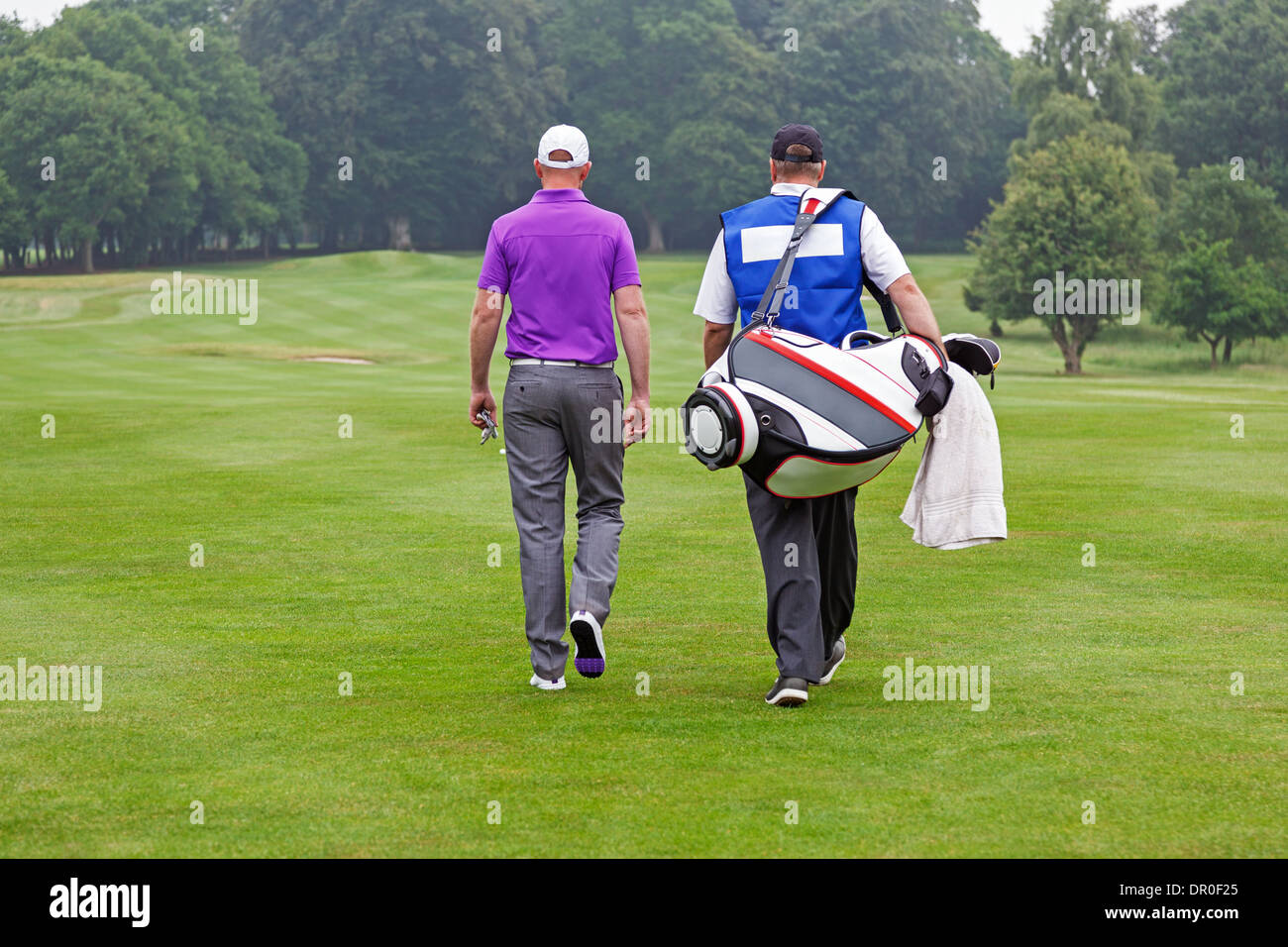 Golfer and caddy walking towards a ball on a par 4 fairway. Stock Photo