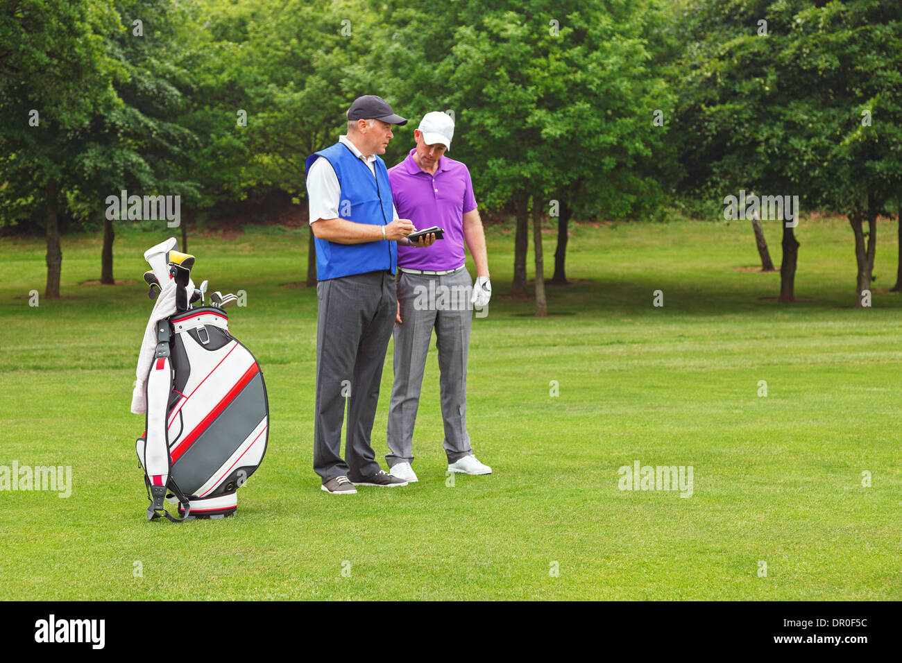 Golfer and caddy standing on the fairway of a par 4 looking at a course guide. Stock Photo