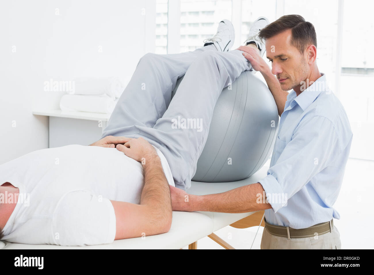 Physical therapist assisting man with yoga ball Stock Photo