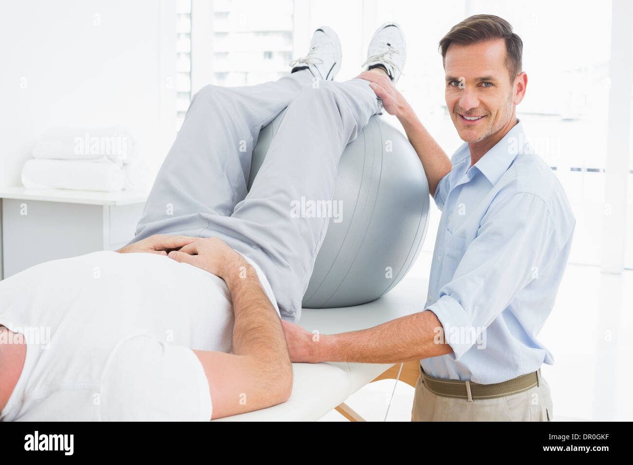 Physical therapist assisting man with yoga ball Stock Photo