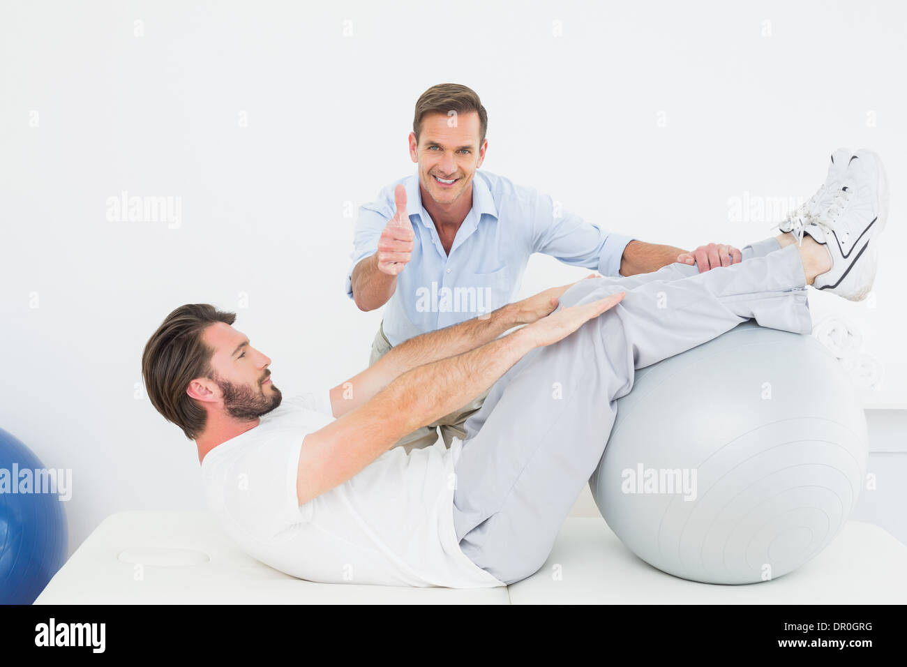 Therapist gestures thumbs up while assisting man do sit ups Stock Photo