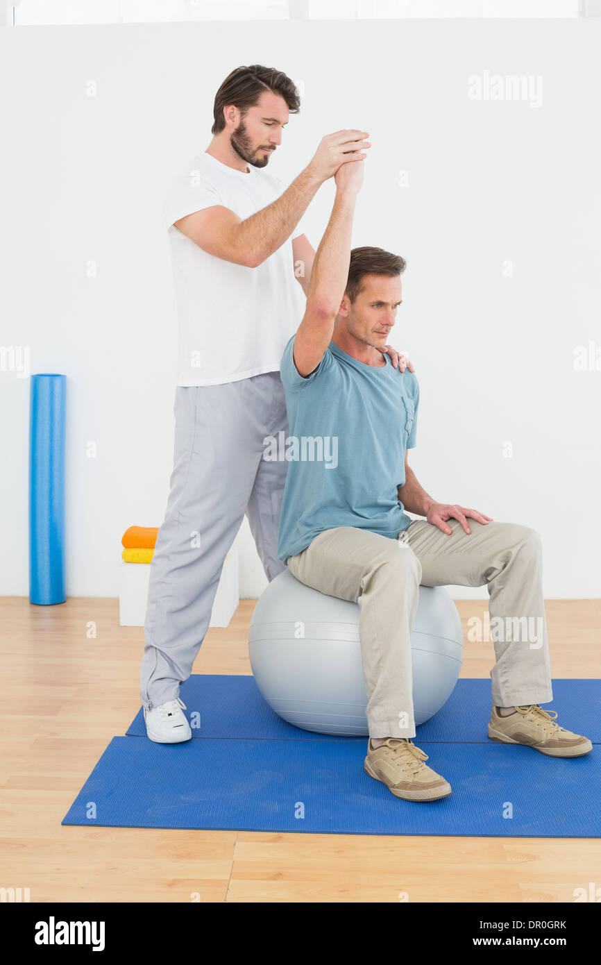 Man on yoga ball working with a physical therapist Stock Photo