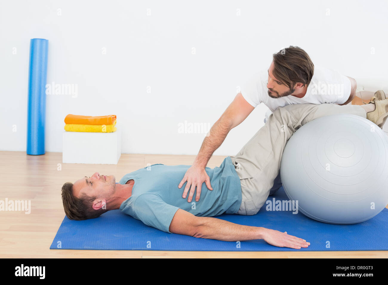 Physical therapist assisting young man with yoga ball Stock Photo