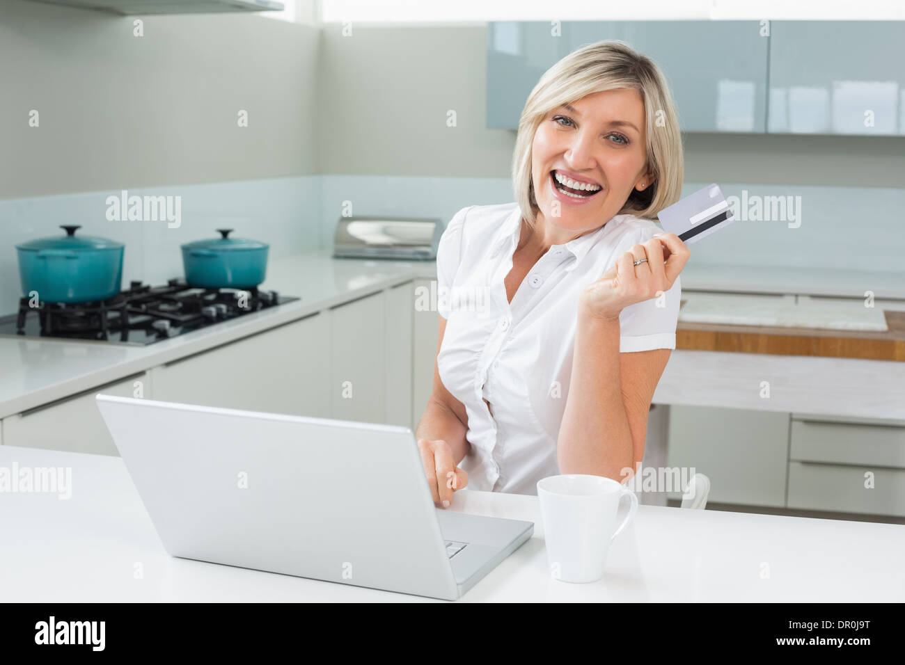 Cheerful woman doing online shopping in kitchen Stock Photo