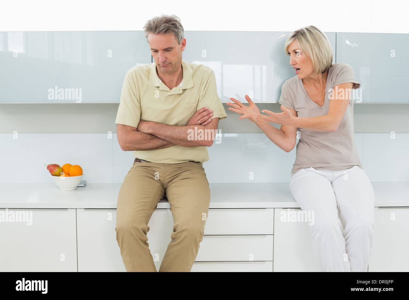 Man with arms crossed as woman argue in kitchen Stock Photo