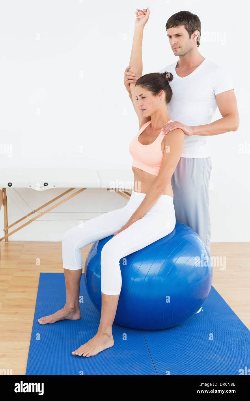 Woman on yoga ball while working with physical therapist Stock Photo