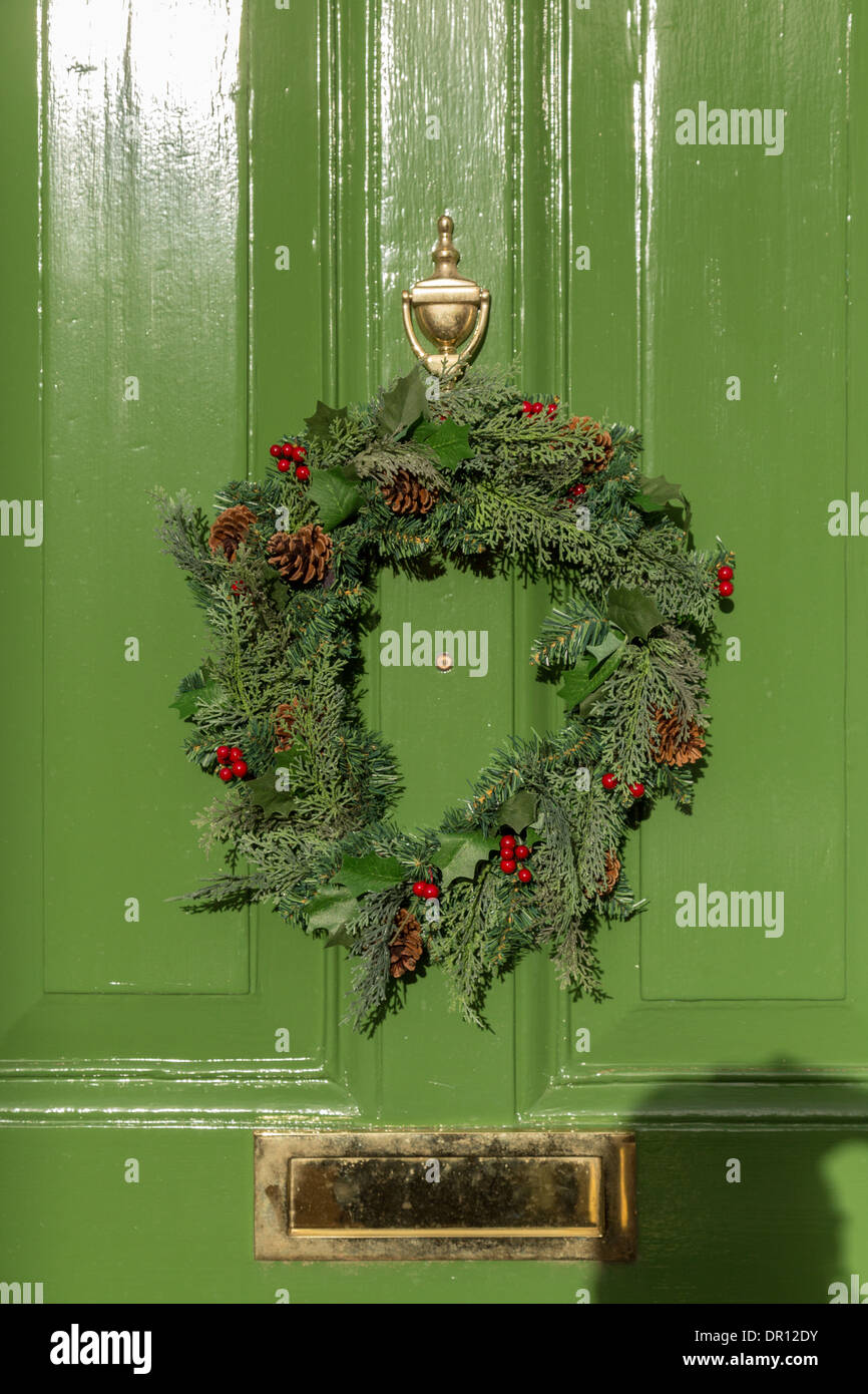 Green front door of traditional English Georgian House. Christmas laurel reef with red berries hung on door. Stock Photo