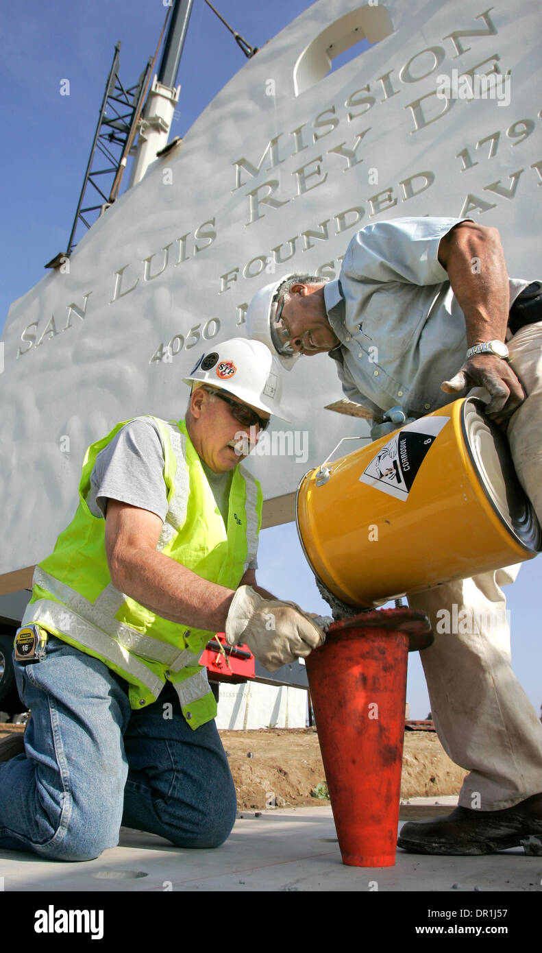 December 4, 2008, Oceanside, California, USA_GEORGE SCHULTZ, left and ALEX JOHNSON, at right, pour a special anchor bolt grout into holes drilled into the base of the Mission San Luis Rey's new 12 foot tall concrete sign. Steel coil rods installed vertically into the base of the sign section suspended behind them will go into the holes when the section is placed on to the base_Cred Stock Photo