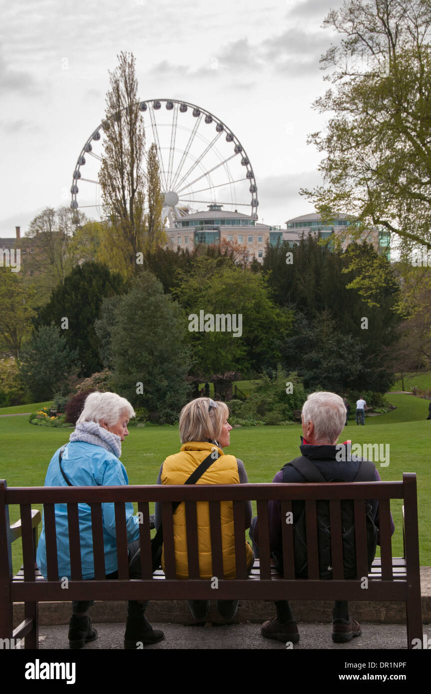 Rear view of 3 grey-haired adults sitting together on park bench, chatting, relaxing & admiring beautiful scenery - Museum Gardens, York, England, UK. Stock Photo