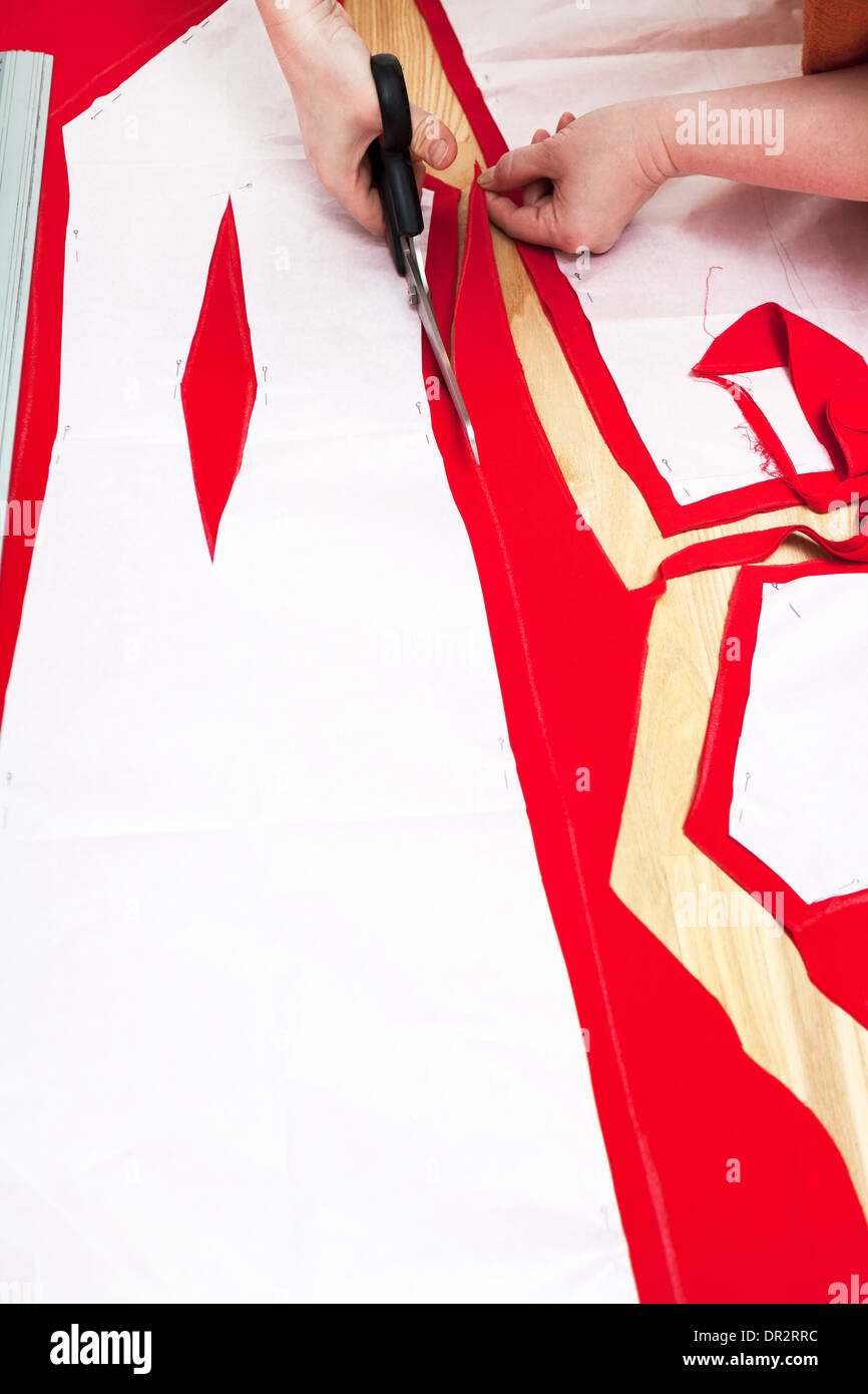 dressmaker cut out woolen fabric along pattern lines for tailoring red