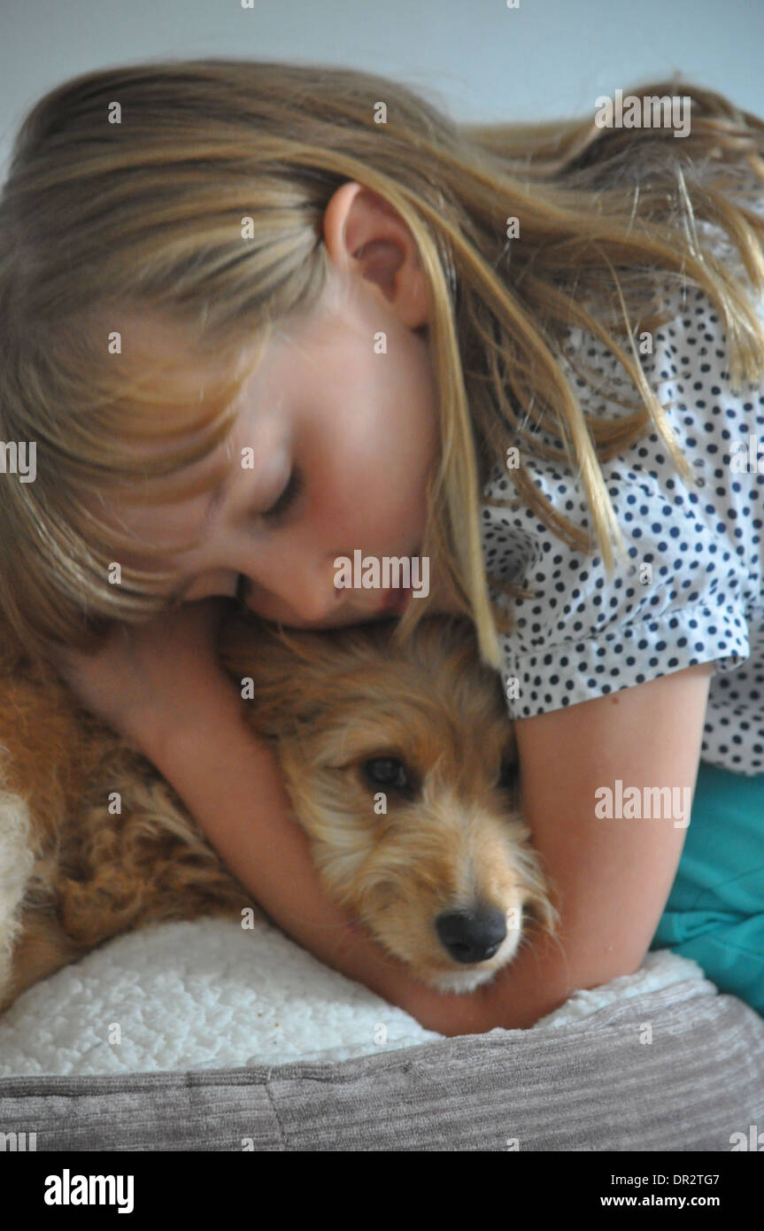 portrait of little blonde girl shutting her eyes in joy as she hugs her pet puppy Cockapoo Stock Photo