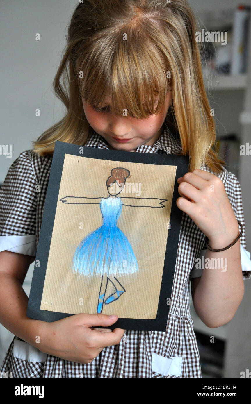little girl looking down at her picture of a blue ballerina and dreaming of being a ballet dancer when she grows up Stock Photo