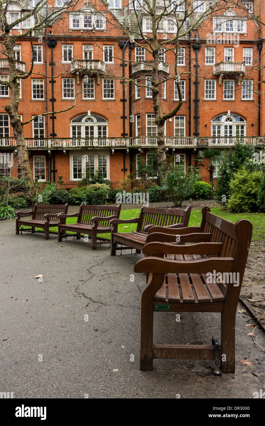 Park benches and the distinctive red brick housing of South Audley Street as seen from Mount Street Gardens Stock Photo