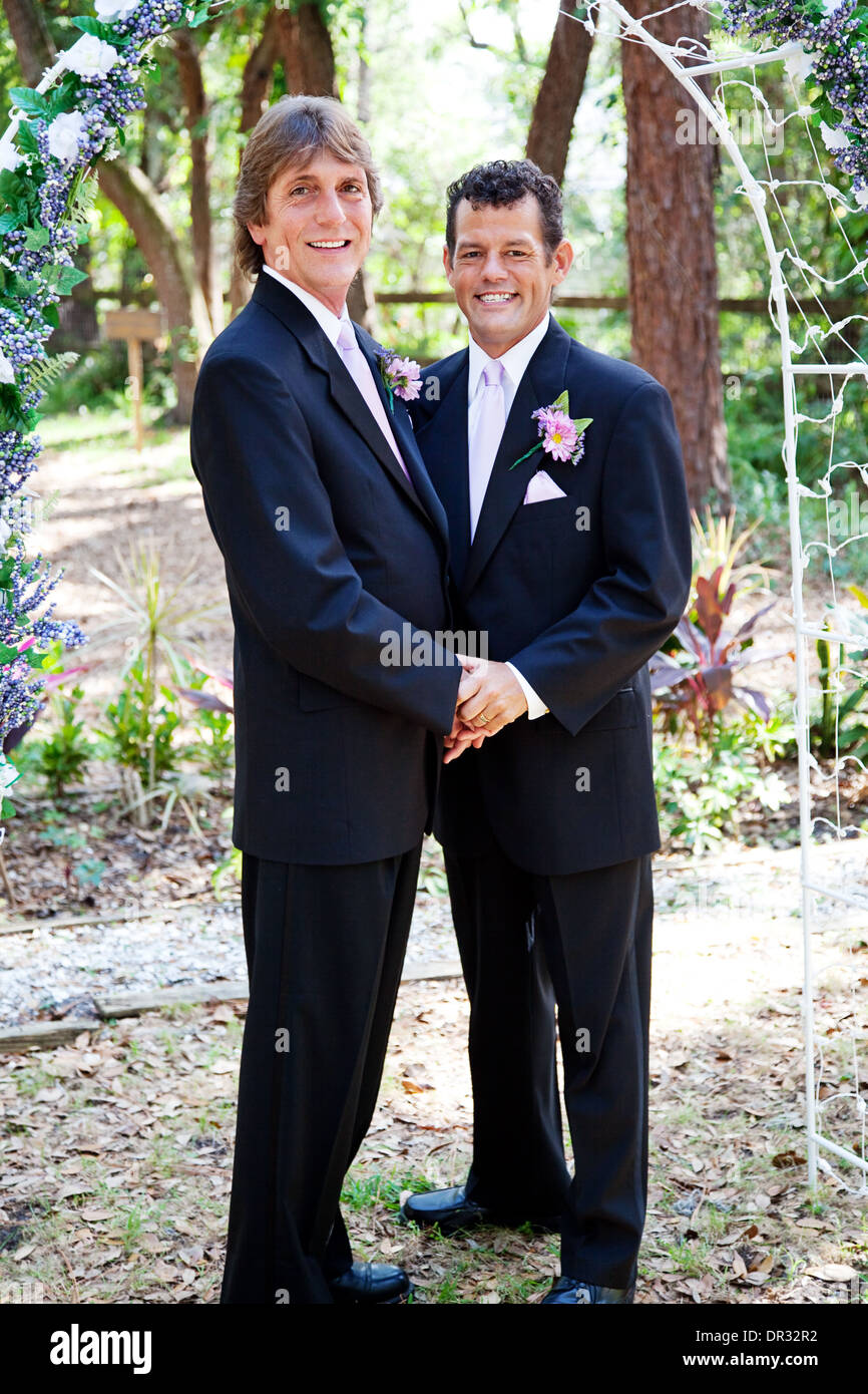 Handsome gay male wedding couple standing under a beautiful floral archway.  Stock Photo