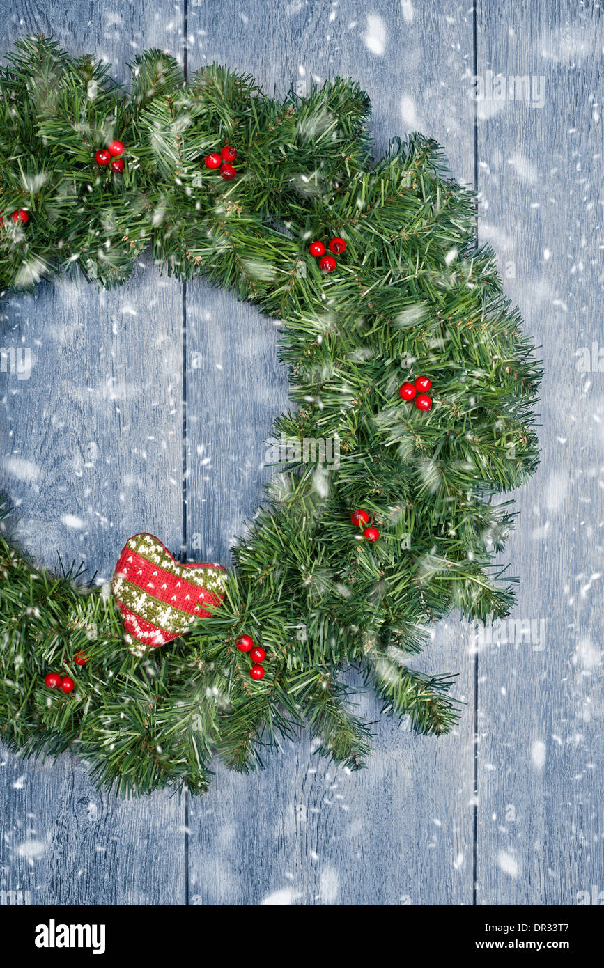 Christmas wreath hanging from rustic door with falling winter snow Stock Photo