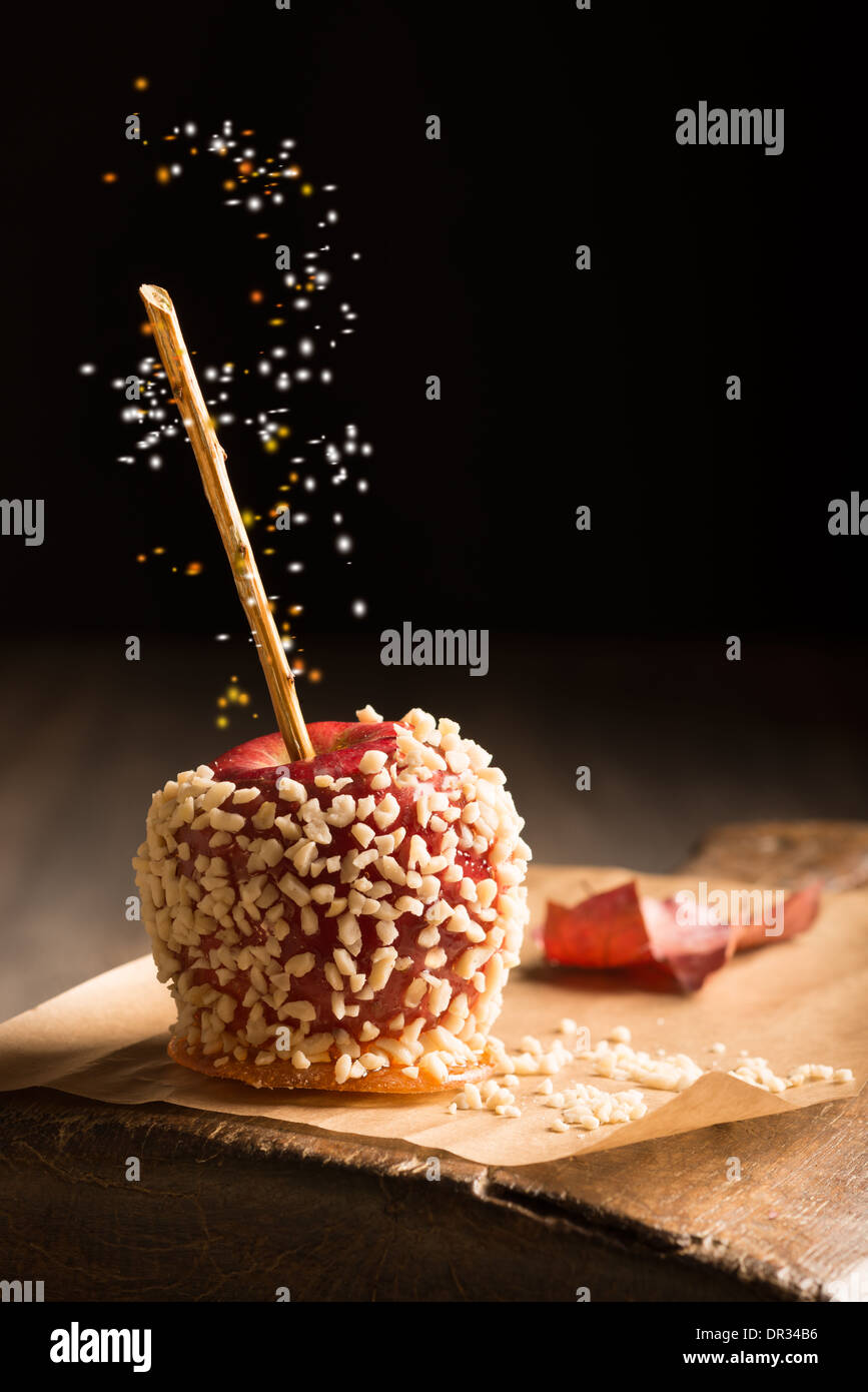 Candy apple covered in chopped nuts on rustic board Stock Photo