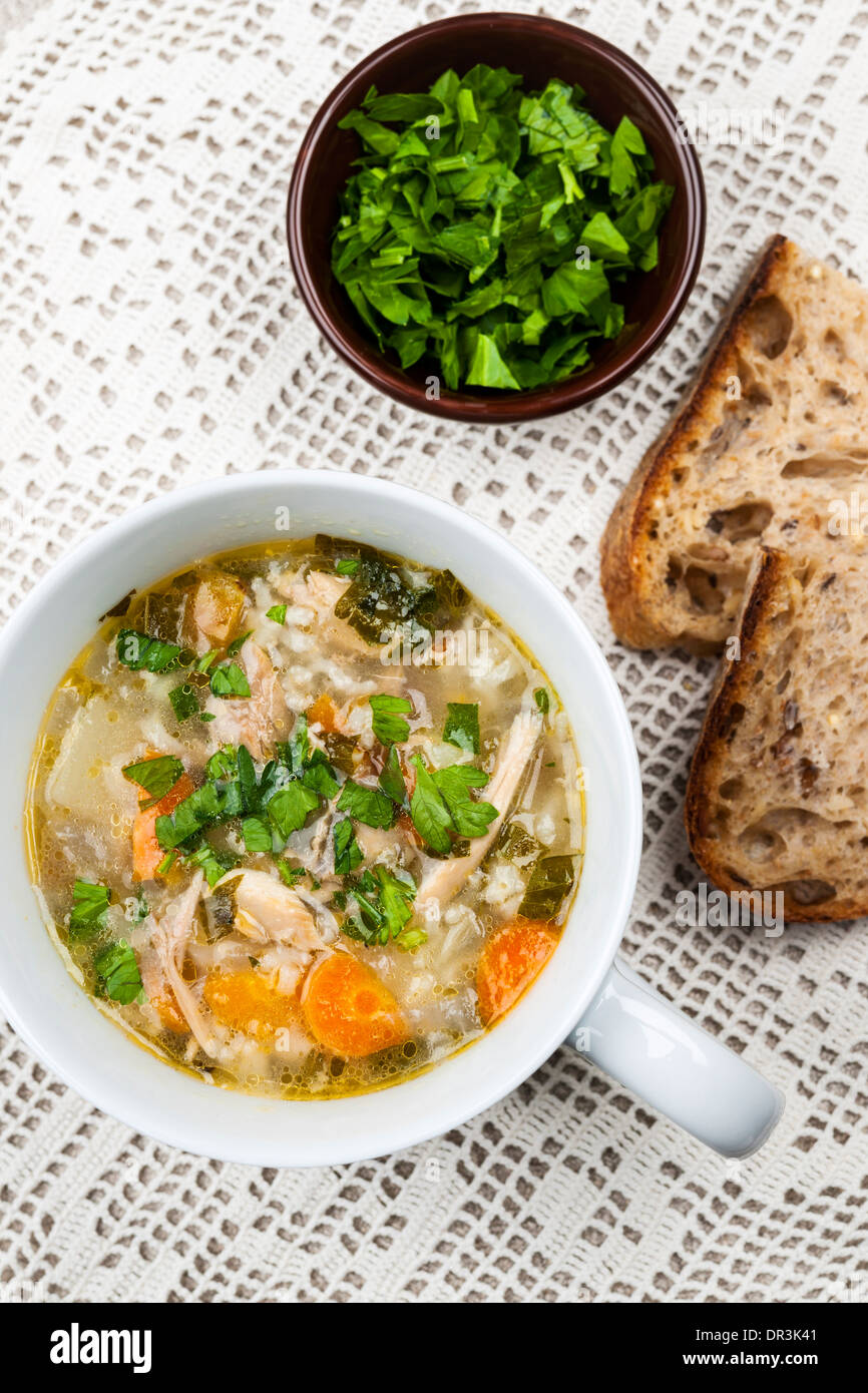 Cup of hot chicken rice soup served with bread and parsley from above on crochet tablecloth Stock Photo