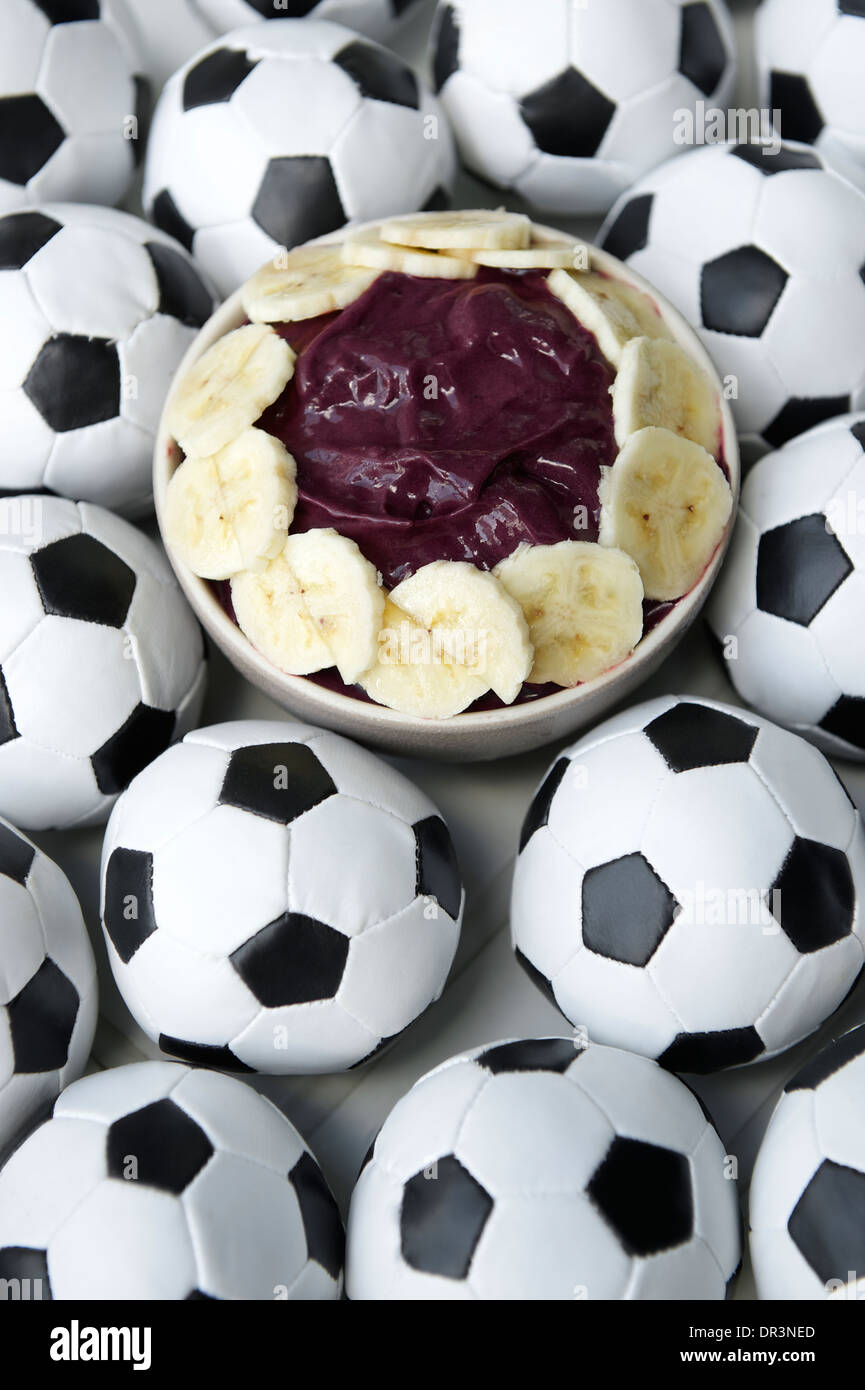 Brazilian culture on the table features a bowl of fresh acai with banana surrounded by football soccer balls Stock Photo