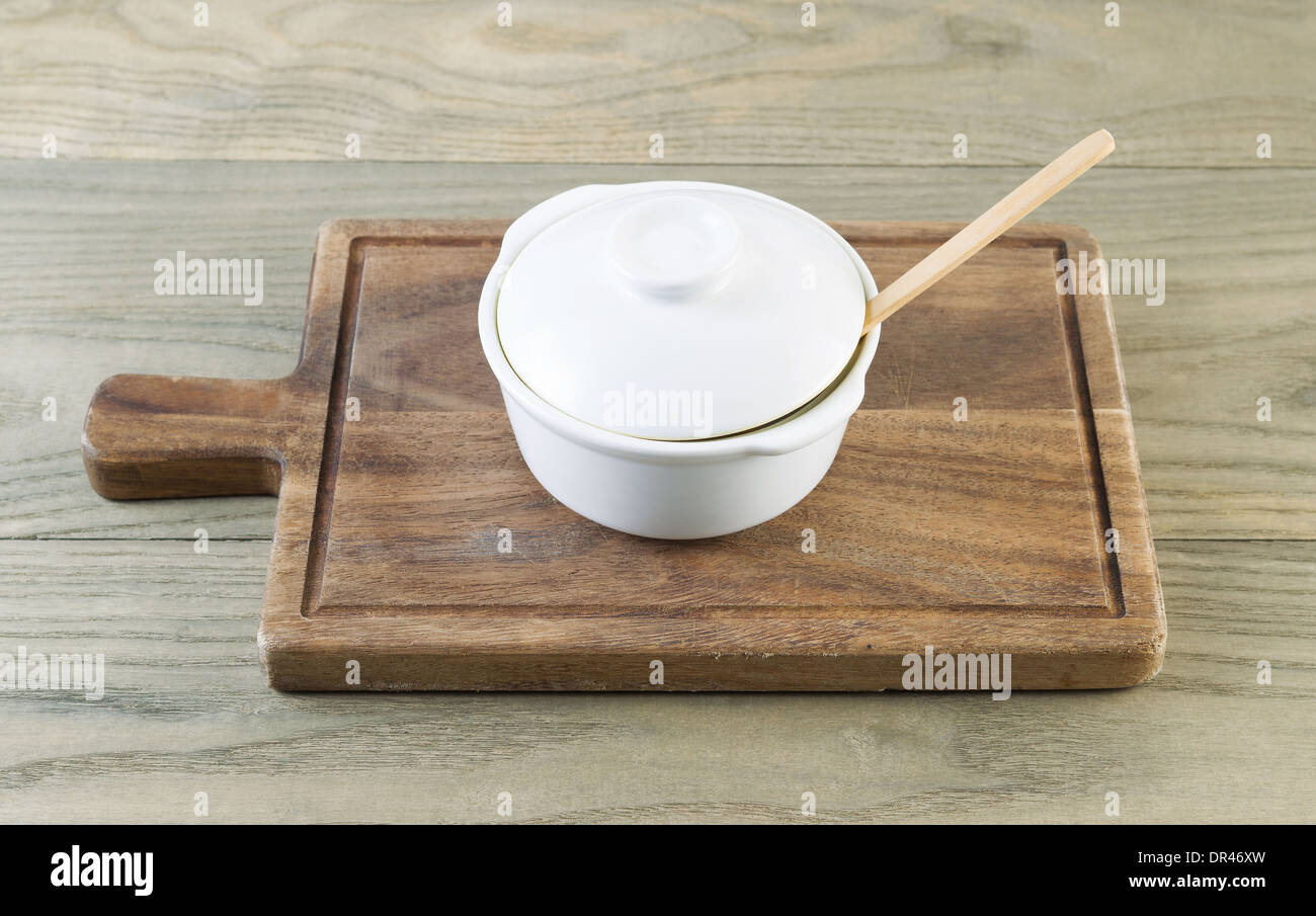 Horizontal photo of white porcelain cooking pot on black walnut serving board with aged wood underneath Stock Photo