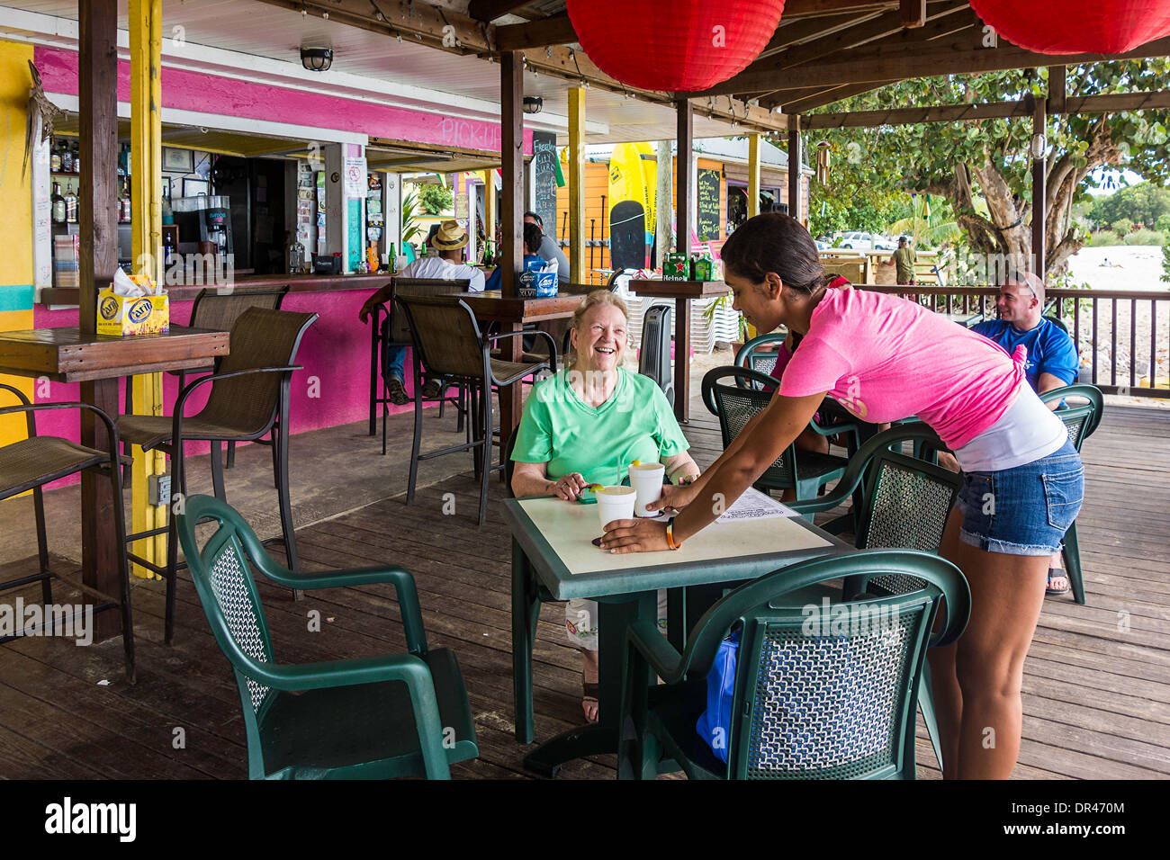 A senior woman interacts with a waitress who is serving margaritas at an outdoor restaurant in St. Croix, U.S. Virgin Islands. Stock Photo