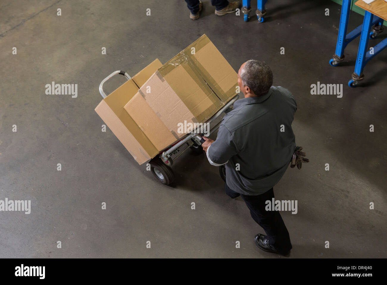 Worker carting boxes on hand truck in warehouse Stock Photo
