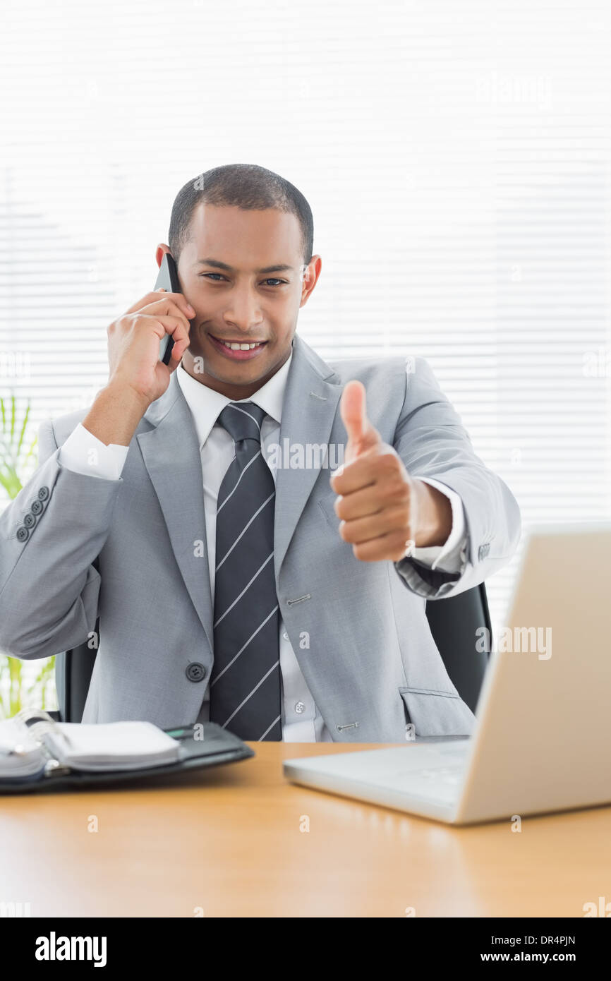 Smiling businessman gesturing thumbs up while on call Stock Photo