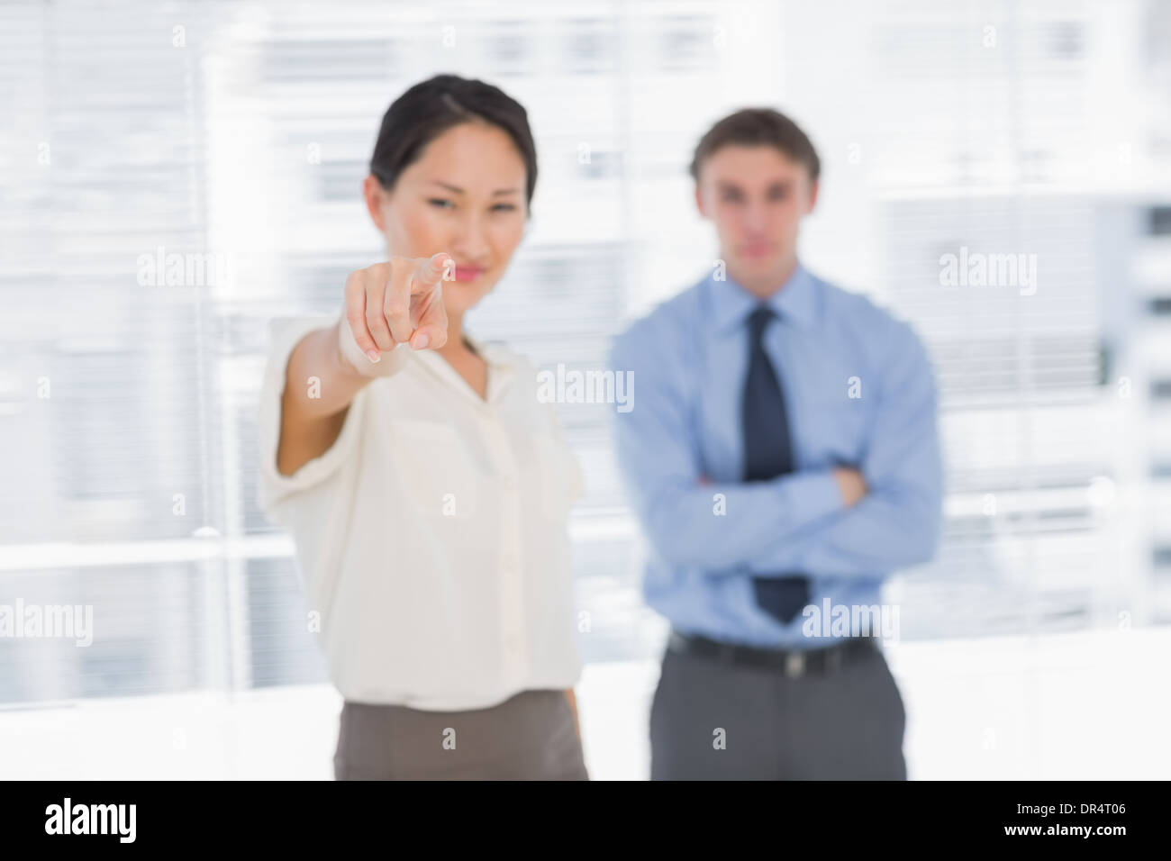 Businesswoman pointing towards camera with man in office Stock Photo
