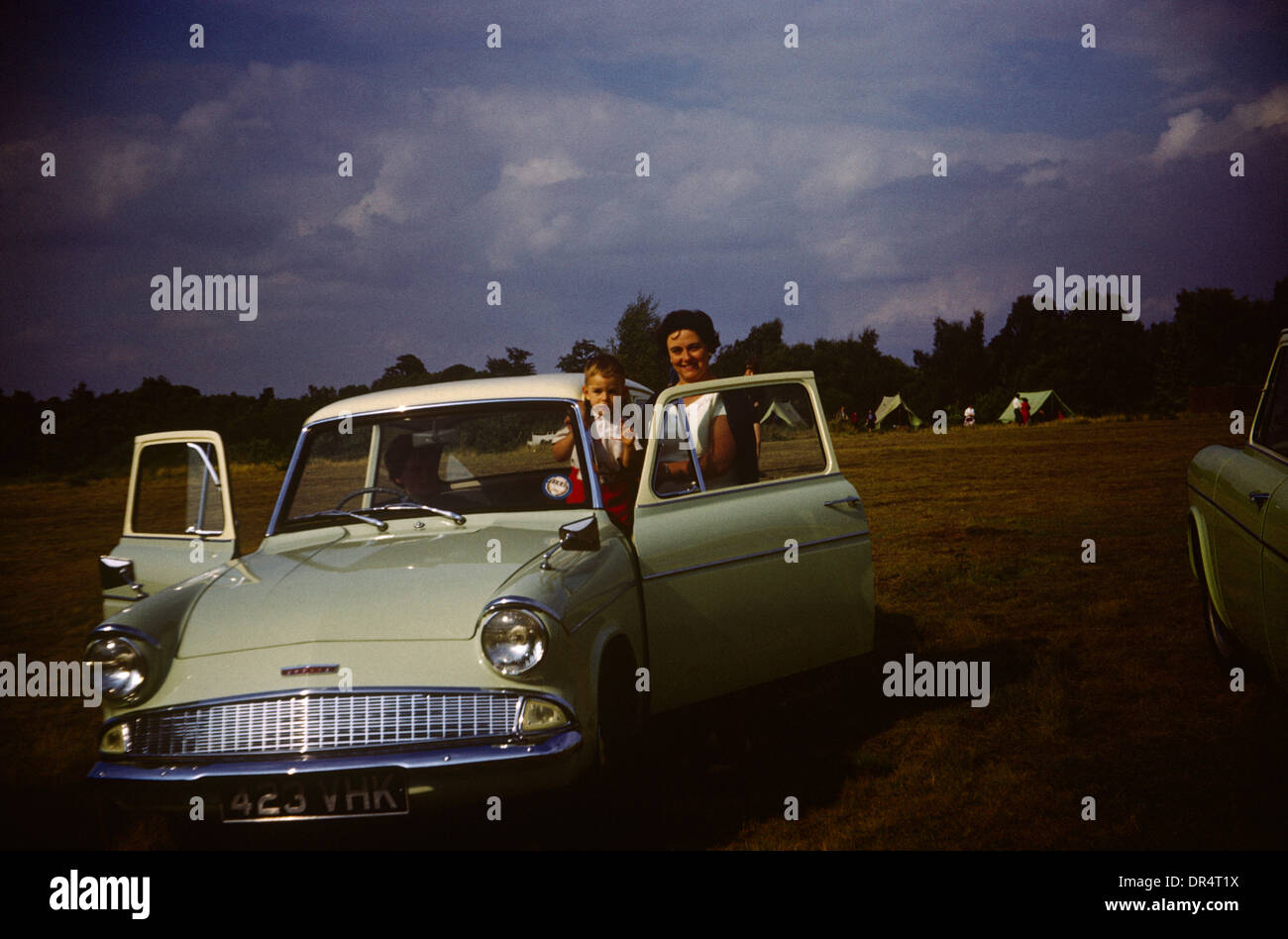A mother holds her 4 year-old son with the family Ford Anglia during summer time in the early 1960s. Stock Photo