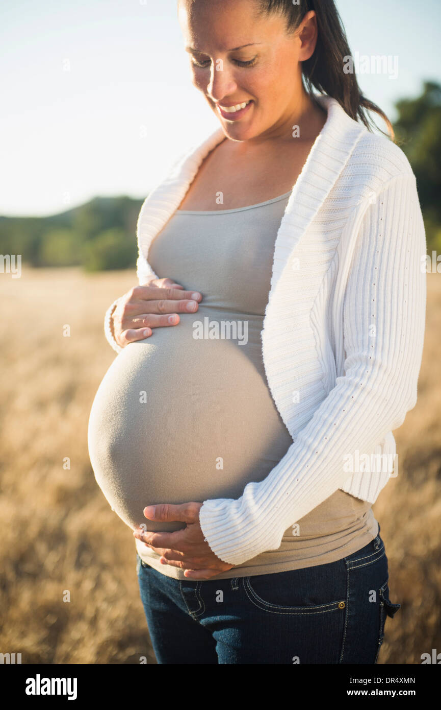 Pregnant Hispanic mother holding stomach in field Stock Photo - Alamy