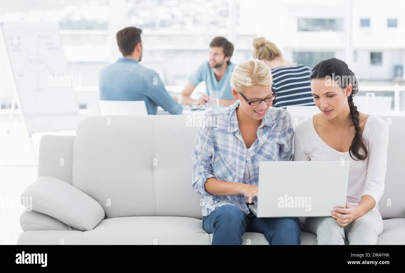 Women using laptop with colleagues in background at creative office Stock Photo