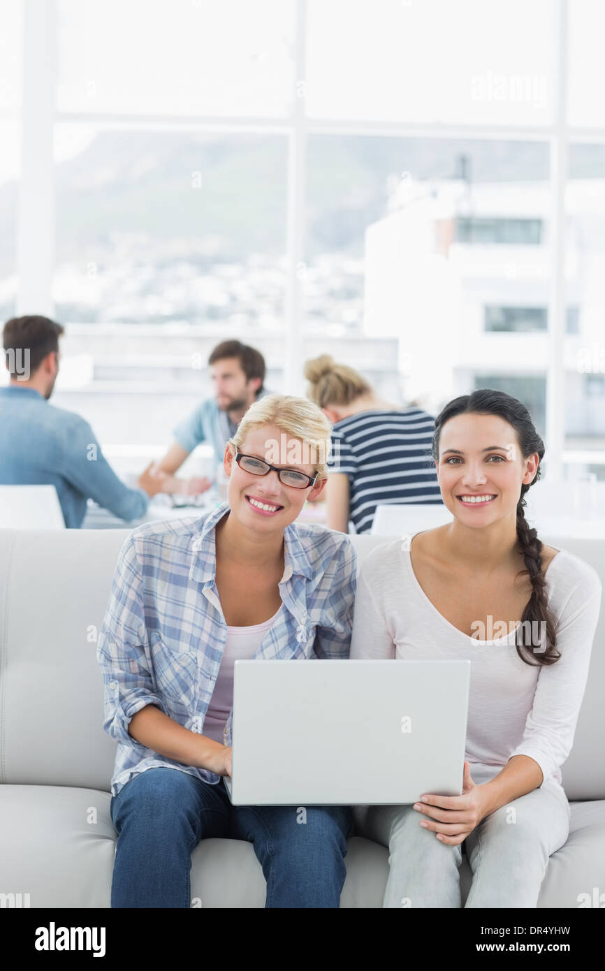 Women using laptop with colleagues in background at creative office Stock Photo