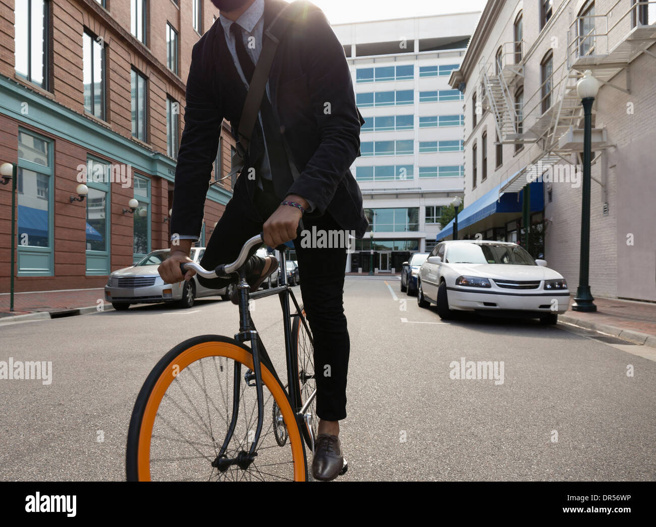 Mixed race businessman riding bicycle on city street Stock Photo