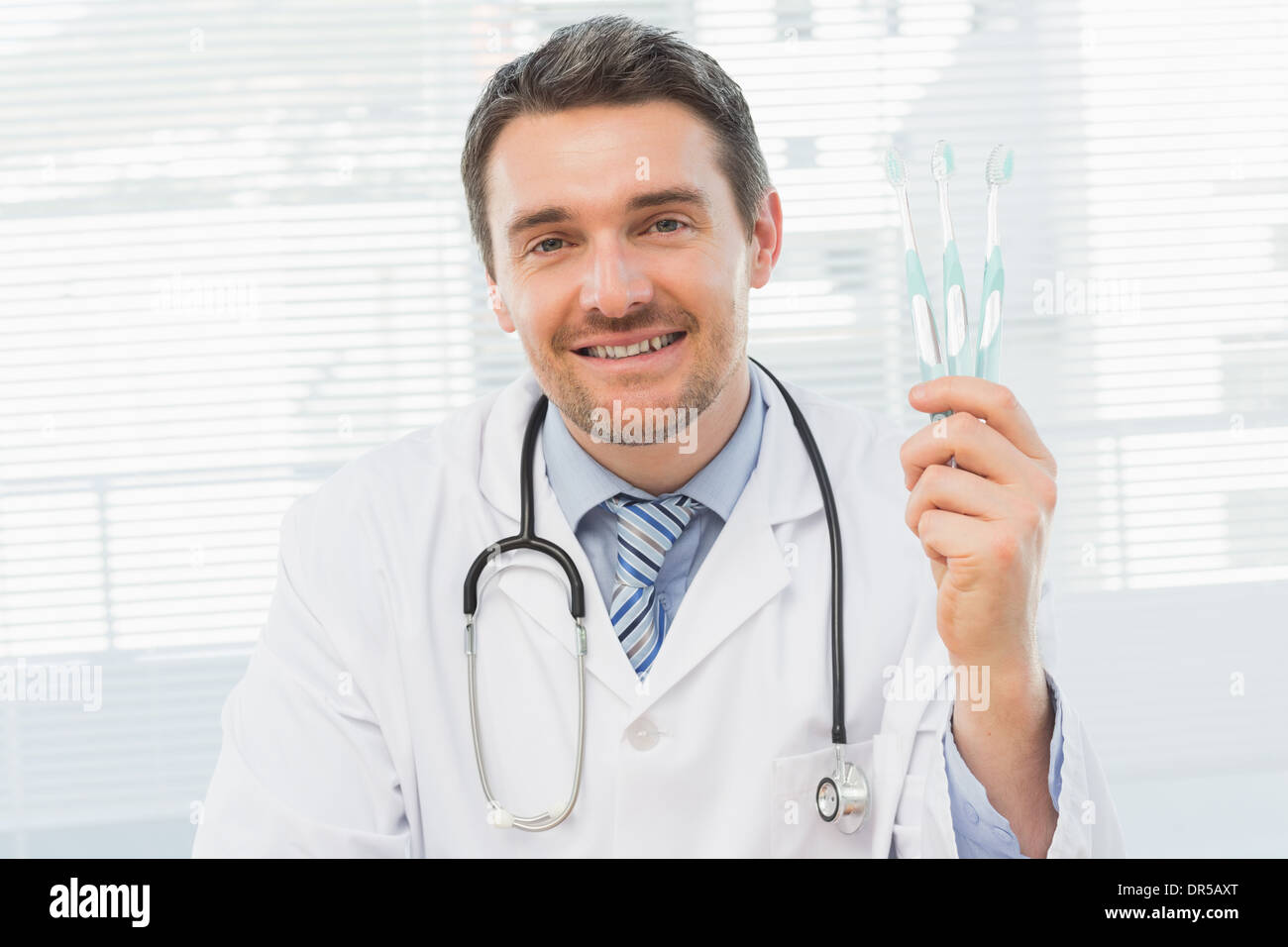 Smiling doctor holding toothbrushes in office Stock Photo