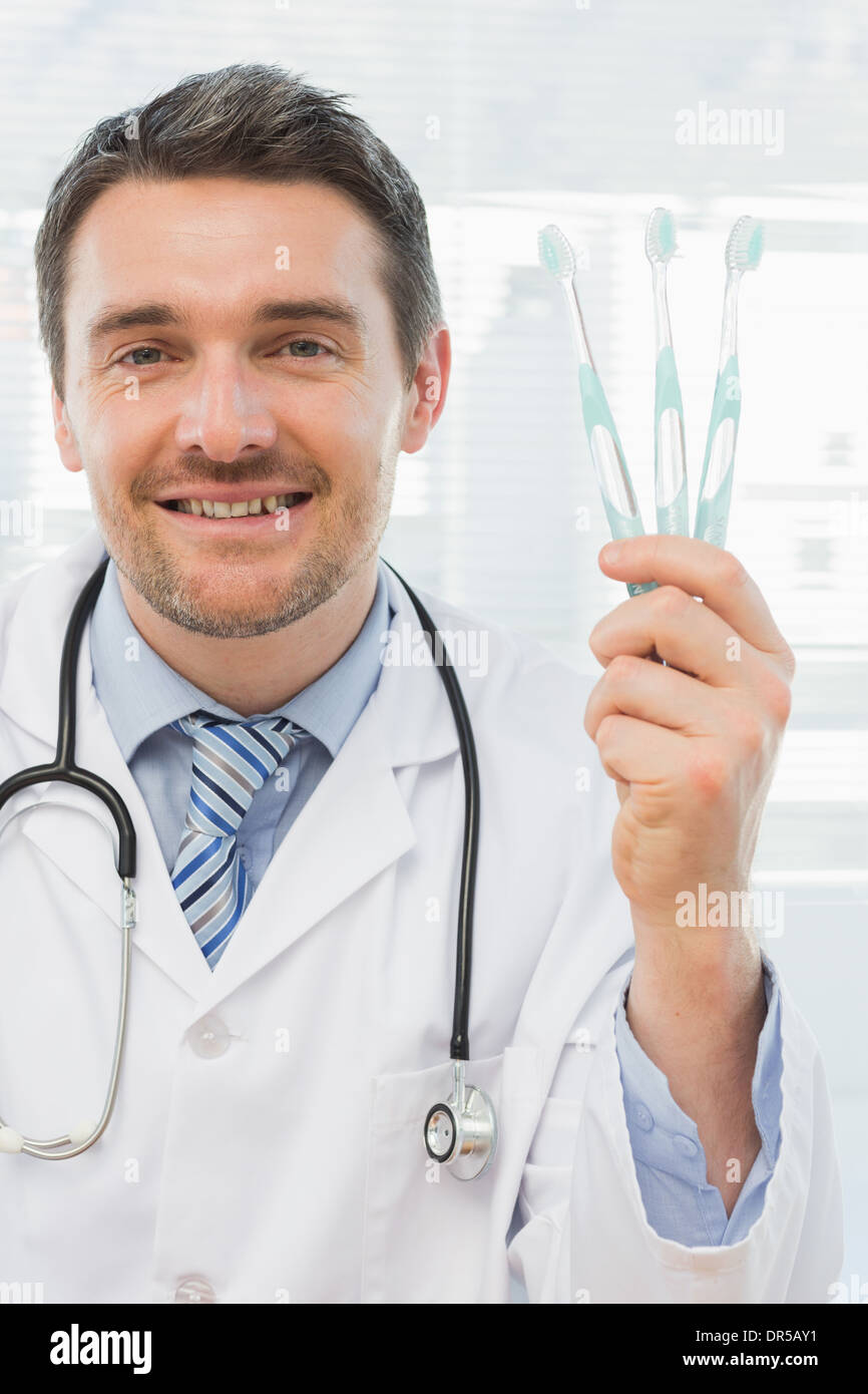 Smiling doctor holding toothbrushes in office Stock Photo