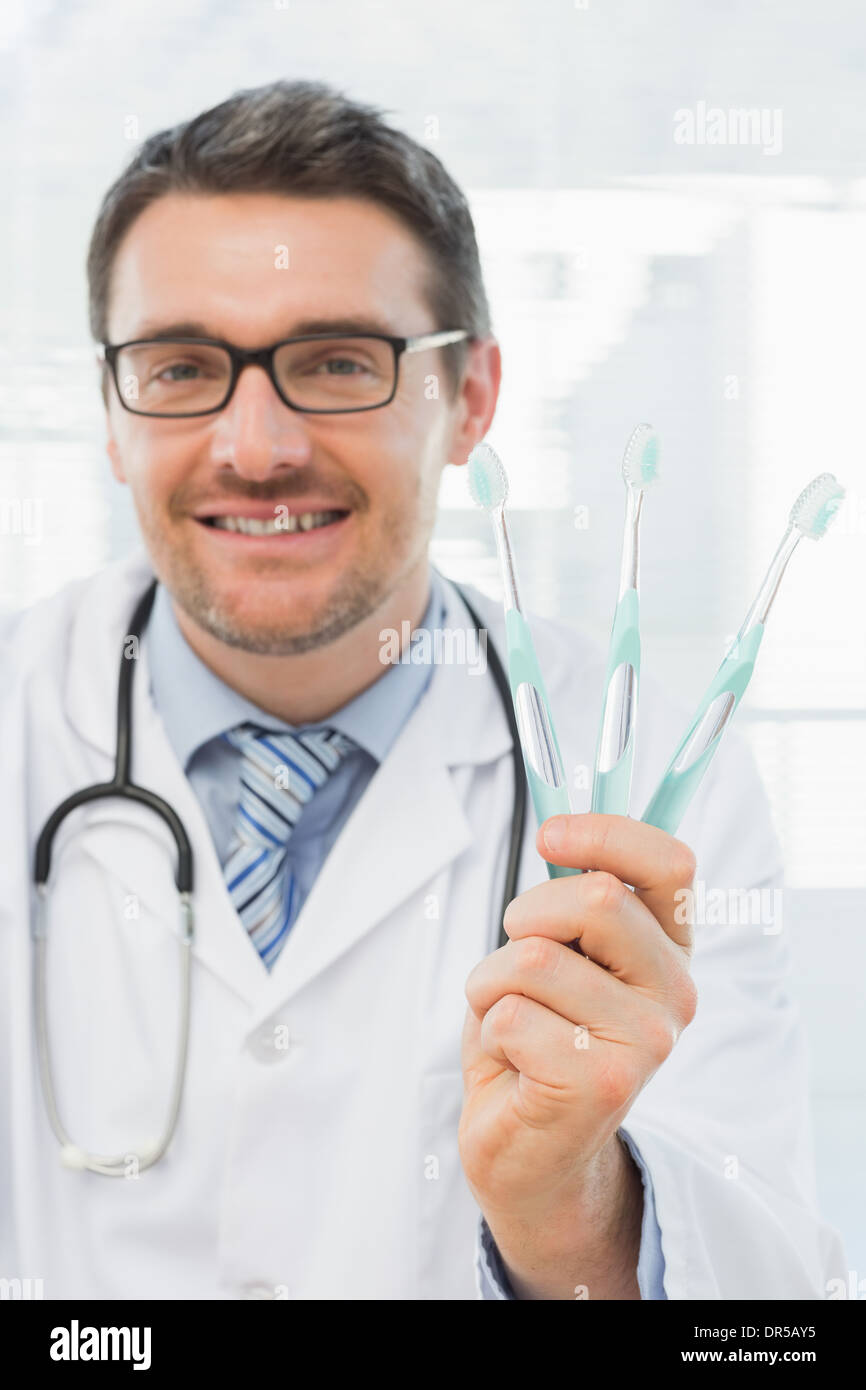 Smiling doctor holding toothbrushes in office Stock Photo