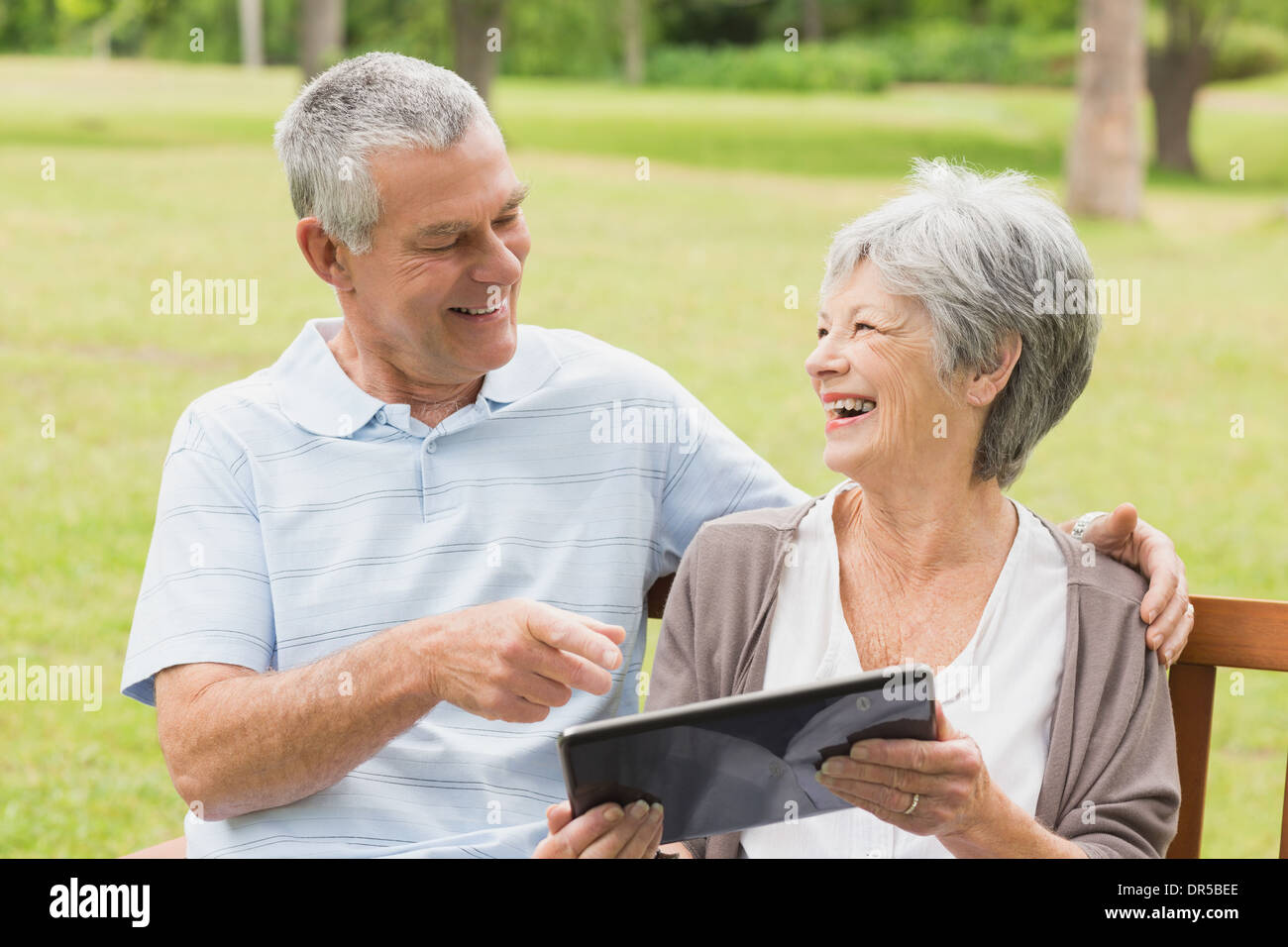 Cheerful senior couple using digital tablet on bench at park Stock Photo