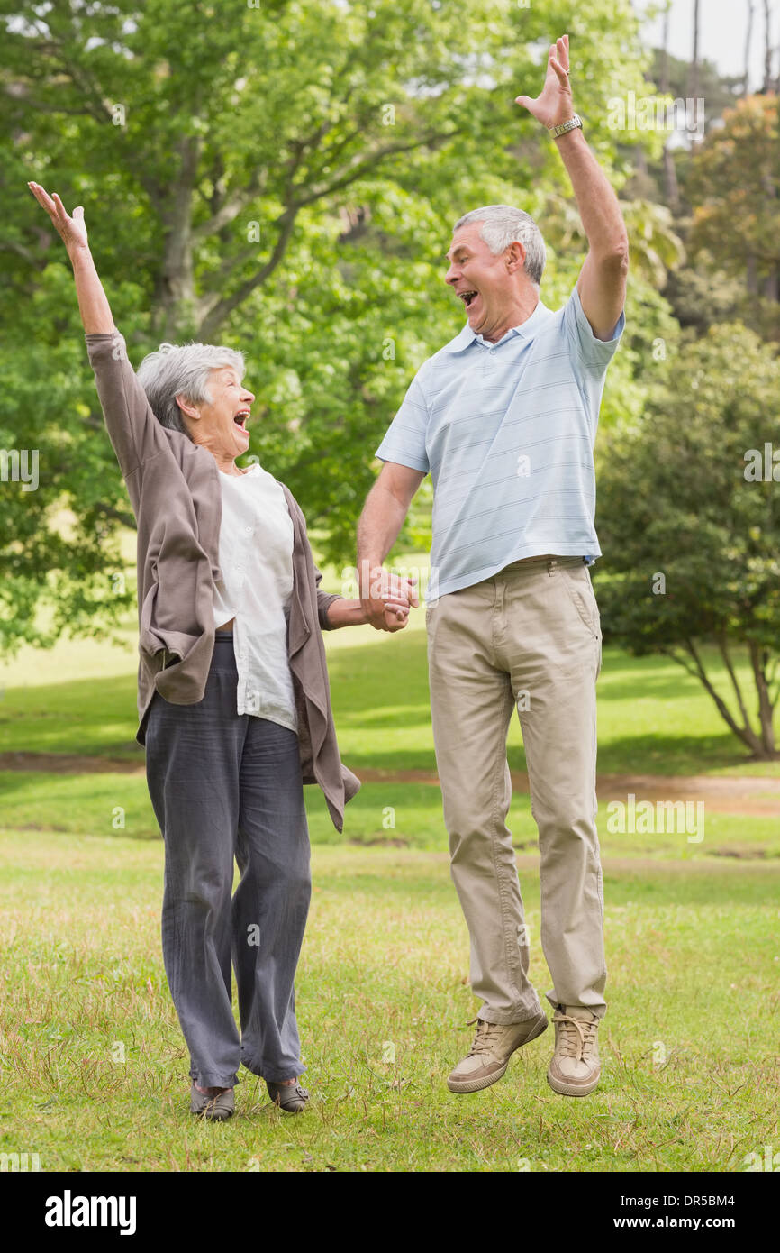 Active senior couple holding hands and jumping in park Stock Photo - Alamy