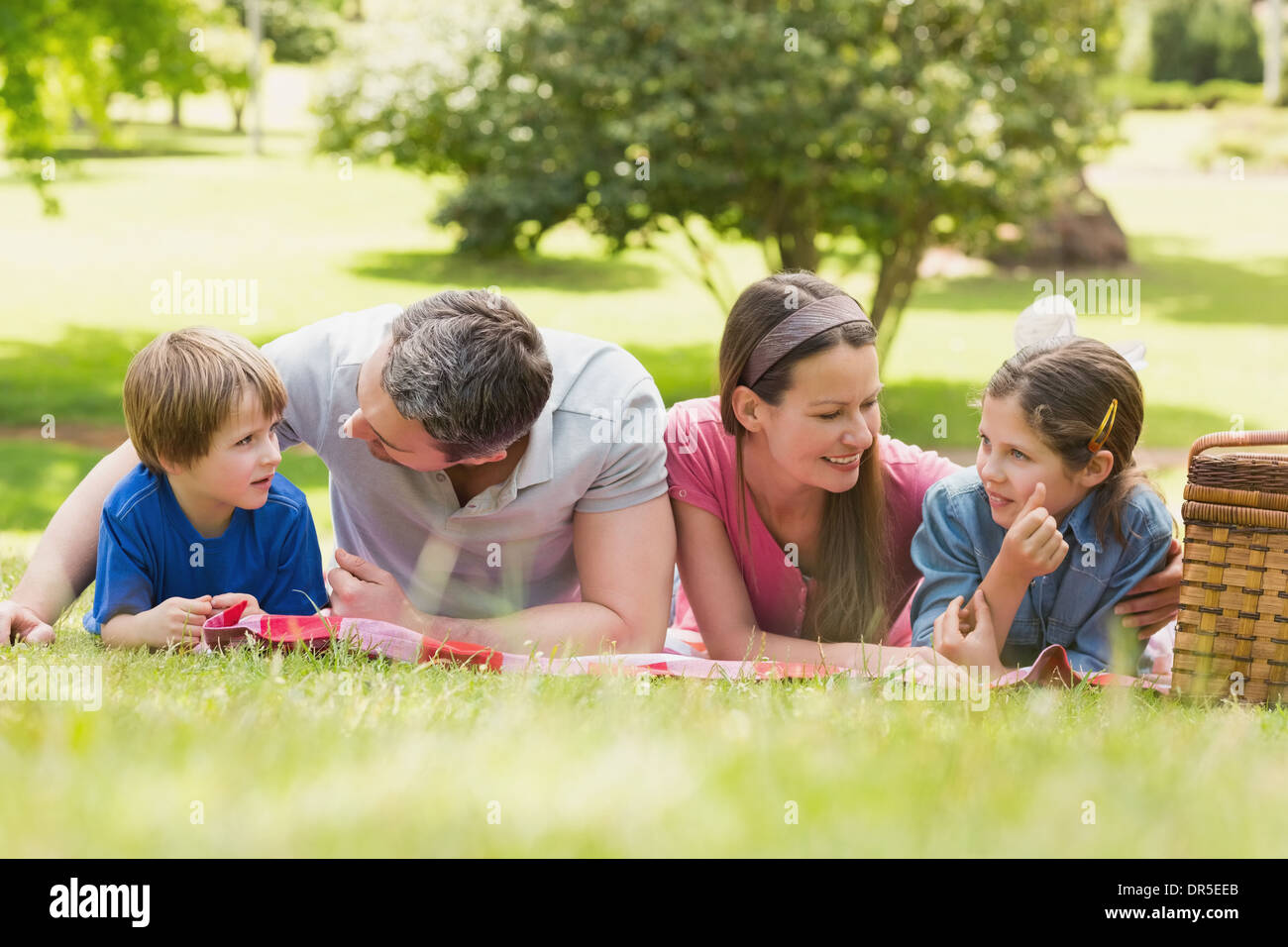 Smiling couple with young kids lying on grass in park Stock Photo