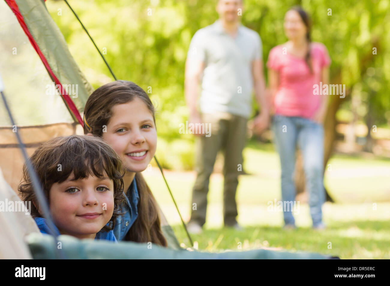 Kids in tent with couple in background at park Stock Photo