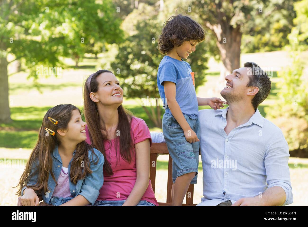 Couple with young kids sitting on park bench Stock Photo
